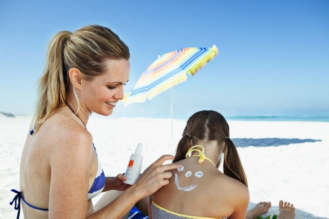 Woman applying sun cream on daughter's (10-12) back